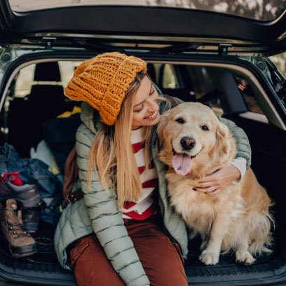 Young woman sitting on the back of her car with her dog during a roadtrip